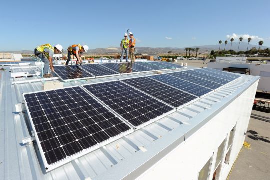 Arbeiter schrauben Solaranlagen auf ein Flachdach.