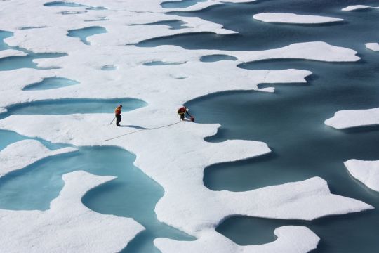 Zwei Forscher laufen in der Arktis auf löchrigem Meereis herum.