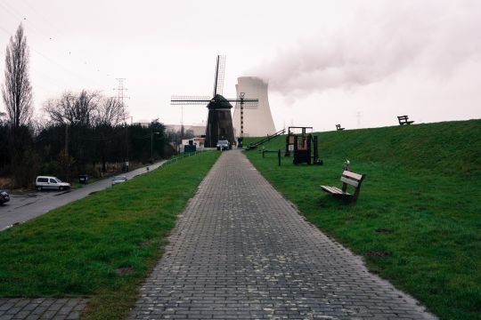 Das Atomkraftwerk Doel in Belgien, vom Deichweg aus betrachtet, hinter einer alten Windmühle stehend.