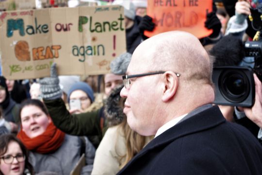 Peter Atlmaier vor einem Plakat mit der Aufschrift "Make our Planet great again", das eine Schülerin hochhält.