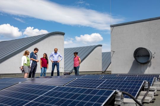 Einige aus dem Verein Solar Powers stehen auf dem Dach zwischen Lüftungsaufbauten und Photovoltaik-Paneelen.