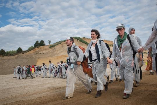 Klimaaktivisten in weißen Maleranzügen laufen Hand in Hand über die Tagebausohle, sie sehen erschöpft, aber zufrieden aus.