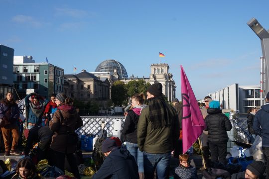 Aktivisten mit Extinction-Rebellion-Flagge auf einer Brücke, im Hintergrund der Reichstag. 
