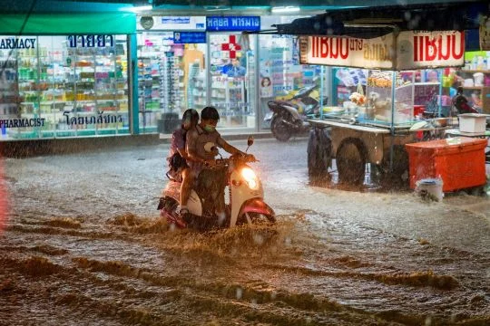 Ein Pärchen auf einem Moped fährt durch überflutete Straßen einer Stadt in Thailand