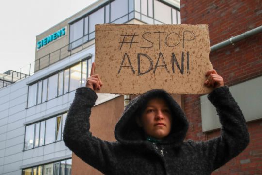 Vor der Siemens-Niederlassung in Dortmund hält eine Klimaaktivistin ein Pappschild hoch mit der Aufschrift "Stop Adani".