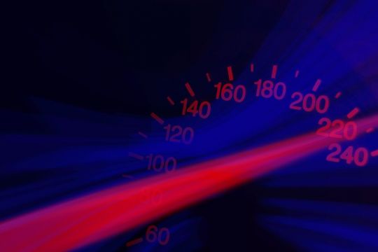 Vor schwarzem Hintergrund zieht sich ein roter Lichtstreifen schräg über das Bild, drum herum etwas blaues Licht und die Anzeige eines Tachometers: über 220 km/h.