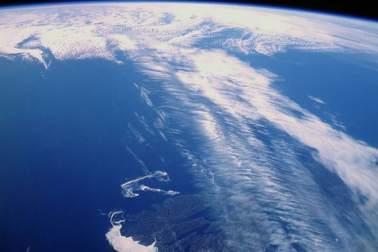Aufnahme aus dem Weltraum: Breites Wolkenband vor blauem Untergrund, im Hintergrund der gekrümmte Erdhorizont.
