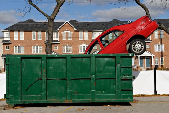 Ein rotes Auto steckt in einem grünen Müllcontainer.