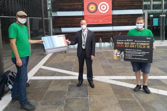 Zwei BUND-Aktivisten mit Mundschutz übergeben dem finnischen Botschafter 40.000 Unterschriften und halten ein Transparent: "Raus aus der Steinzeit – Nein zu Datteln 4!"