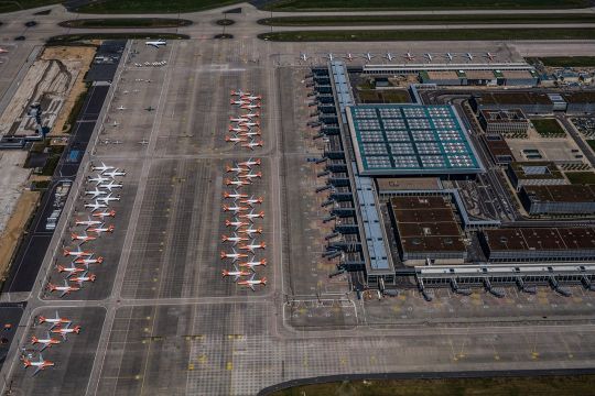 Luftaufnahme vom Flughafen Berlin Brandenburg, zahlreiche Flugzeuge stehen aufgereiht neben der großen Halle.