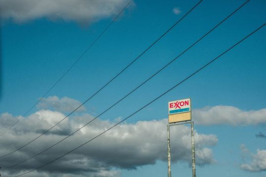 Altes Exxon-Schild vor wolkigem Himmel, Stromleitungen durchziehen das Bild.