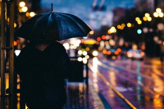 Ein Mensch mit einem Regenschirm geht neben einer Straße.