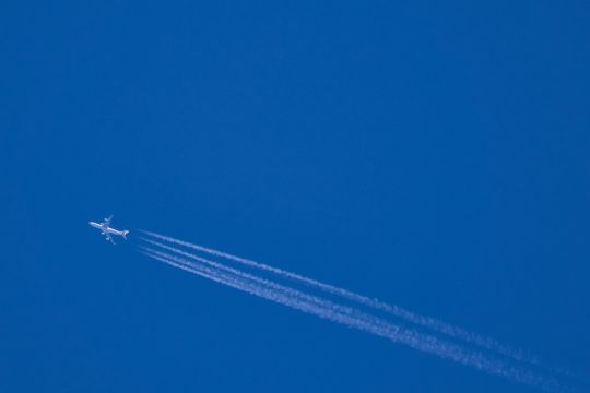 Flugzeug vor blauem Himmel mit Kondensstreifen