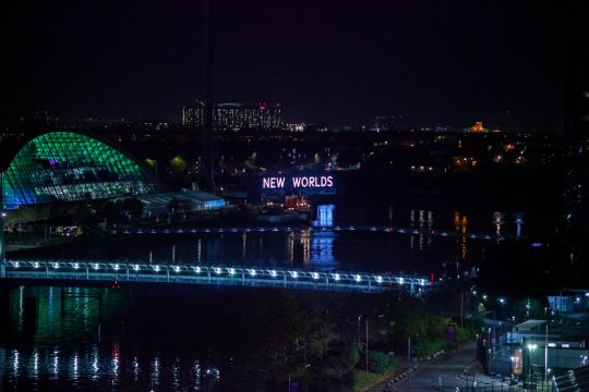 Nachtaufnahme des Konferenzzentrums in Glasgow während des Klimagipfels, daneben ein beleuchteter Schriftzug: New Worlds - Neue Welten.