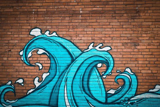 Graffito an einer Ziegelmauer: Zwei türkisfarbene Wellen schlagen hoch.