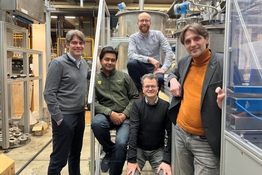 Gruppenfoto: Fünf Männer zwischen labortechnischen Anlagen.