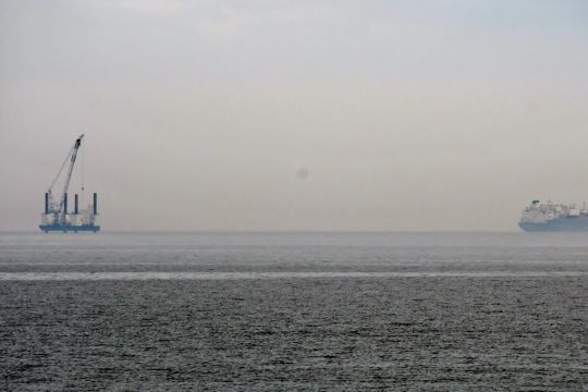 Eine Plattform und in einiger Entfernung ein Schiff etwa einen Kilometer vor der Küste, das Wetter ist diesig.