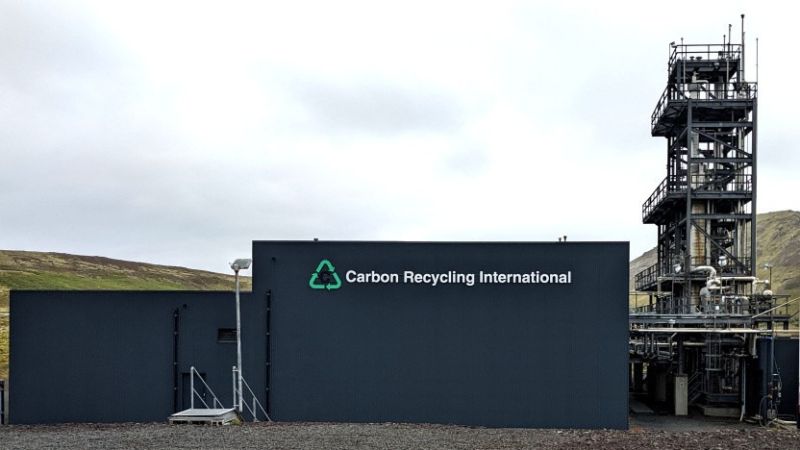 Neben einer kleinen Industrieanlage steht ein nicht sehr großes, dunkelgraues Industriegebäude mit der Aufschrift: Carbon Recycling International.
