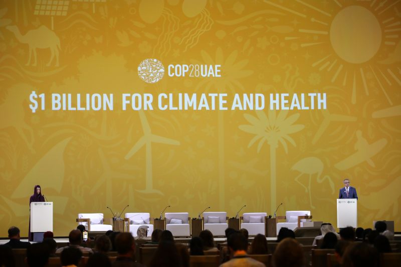 Auf einer Bühne während der COP28 stehen zwei Personen. Dahinter an der Wand steht groß $1 Billion for Climate and Health.