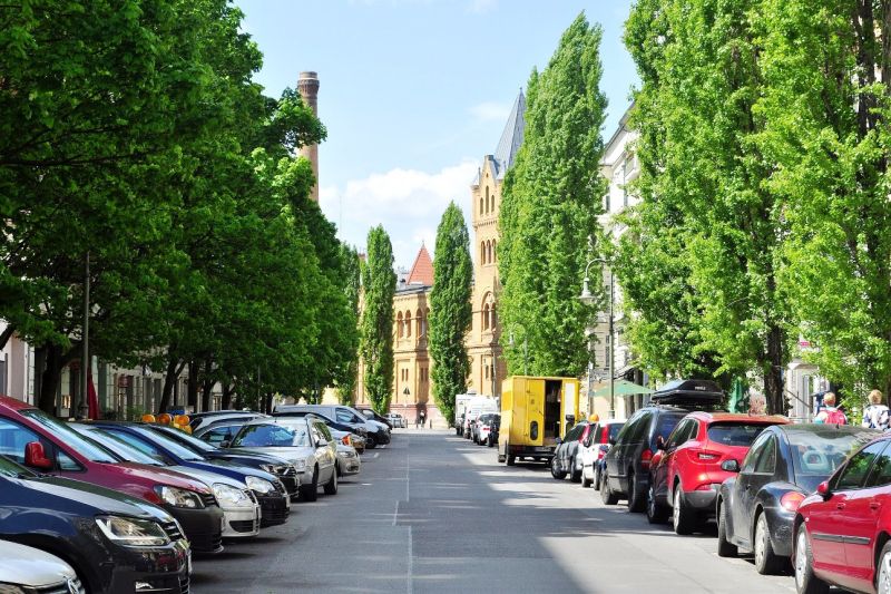 Blick entlang einer Straße in Berlin-Prenzlauer Berg, die beiderseits von Bäumen und Autos gesäumt ist.