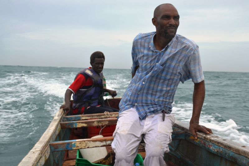 Zwei Fischer fahren auf einem kleinen Fischerboot mit Außenbordmotor über das Meer.