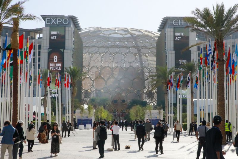 Menschen gehen auf das Konferenzzentrum des Klimagipfels in Dubai zu.