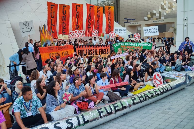 Bunte Sitzdemonstration mit einigen Dutzend Menschen aus vielen Ländern und Transparenten gegen fossile Energien.