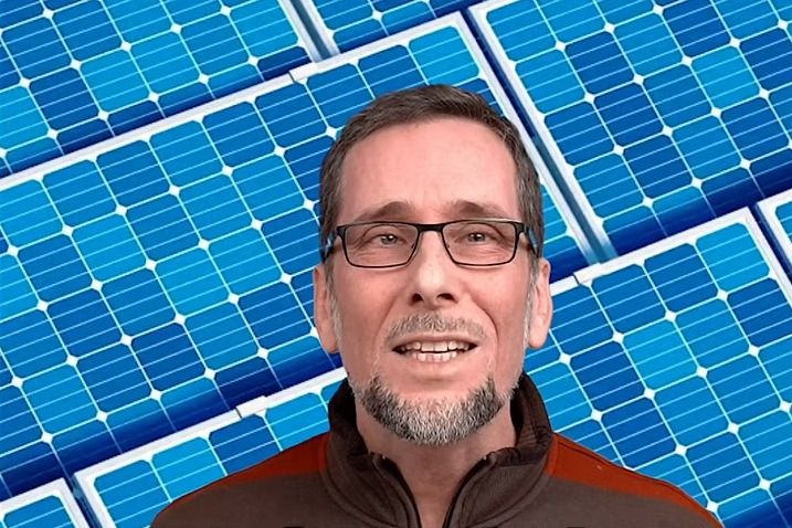 Aufmacherbild: Volker Quaschning in quer gestreifter Trainingsjacke, der Hintergrund besteht aus Solarpaneelen, in denen die Module in leicht unterschiedlichen Blautönen leuchten.