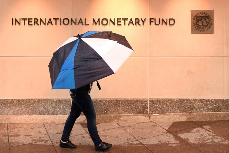 Eine hinter einem Schirm verborgene Person geht bei Regen am Gebäude des IWF in Washington vorbei.