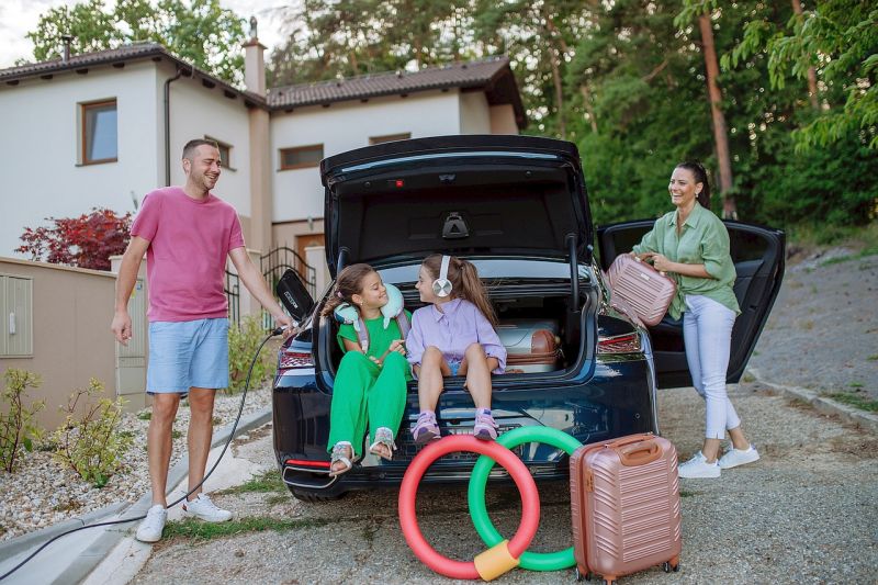 Eine junge Familie mit zwei Kindern ist dabei, von ihrem Einfamilienhaus mit dem Elektroauto in den Urlaub zu fahren.