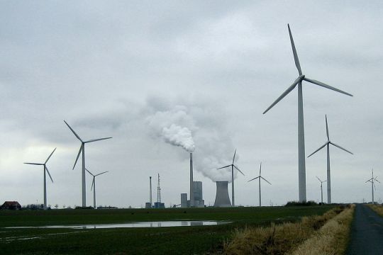 Das Bild zeigt ein Kohlekraftwerk. Im Vordergrund stehen einige Windräder. 