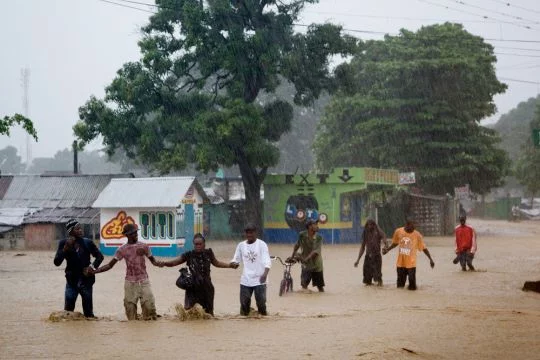 Das Foto zeigt eine Straßenszene in Haiti. Nach einem Hurrikane sind die Straßen überflutet, Menschen stehen knietief im Wasser.