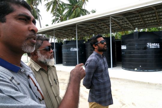Hier ist der Inselrat von Maabaidhoo Island zu sehen. Die Männer zeigen die Tanks, mit denen Regenwasser gespeichert wird, damit die Wasserversorgung auch in der Trockenzeit sicher ist.