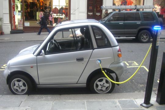 Ein kleines Elektroauto steht am Straßenrand und wird an einer Ladesäule aufgeladen.