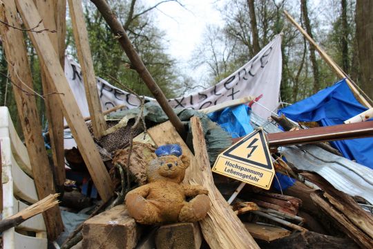 Barrikade aus Holzlatten, -balken und Gerümpel vor Waldbäumen, darauf ein gelbes Wanrschild 