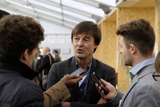 Nicolas Hulot, umringt von Reportern und deren Mikros, vor Wänden aus Spanplatten, wie sie für das Konferenzzentrum der COP21 typisch waren
