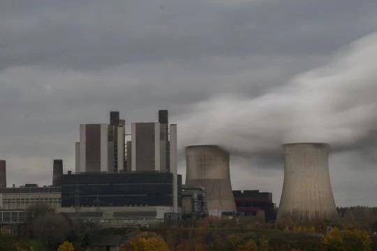 Ein riesiges Kraftwerk mit zwei dampfenden Kühltürmen vor wolkenverhangenem Himmel.