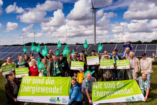 Eine größere Menschengruppe mit Bürgerenergie-Plakaten vor Solar- und Windanlagen