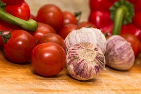 Knoblauch, Tomaten und Paprika liegen auf einem Tisch.