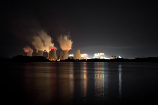 Sechs dampfende Kraftwerks-Kühltürme bei Nacht, aus der Entfernung über einen See aufgenommen.