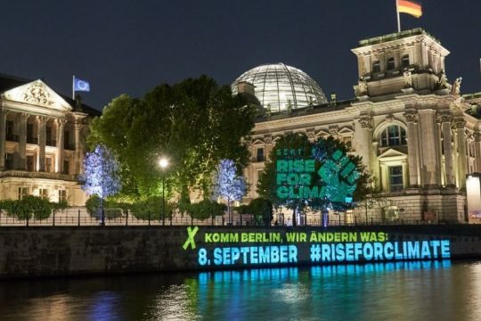 Auf die Ufermauer am Reichstagsgebäude ist nachts ein Slogan projiziert: "Komm, Berlin, wir ändern was: 8. September – Rise for Climate".