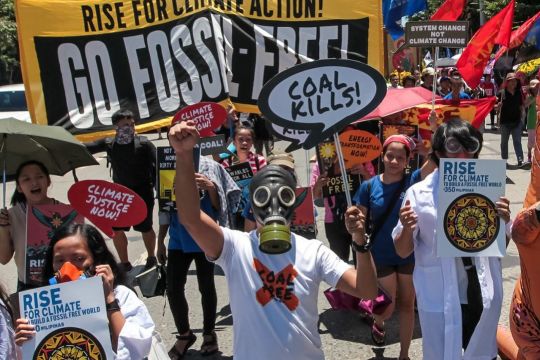 Menschen mit Gasmasken in einem Demonstrationszug, auf Transparenten steht 