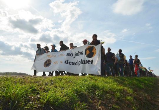 Langer Demonstrationszug mit Transparent "There are no jobs on a dead planet" auf einem Feldweg.