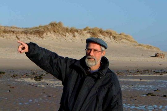 Karsten Reise steht am Strand von Sylt und zeigt auf die gefährdete Küstenlinie.