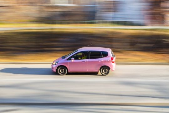 rosa Auto fährt schnell auf einer Straße, Hintergrund unscharf