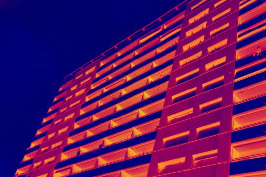 Wärmebild einer Hochhausfassade von schräg unten in Violett über Rot bis Gelb.