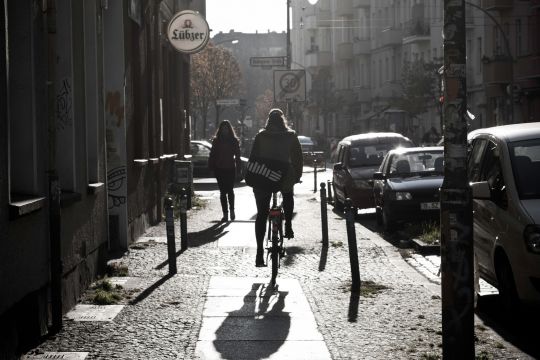 Zwei Fahrradfahrer begegnen sich auf einem Bürgersteig, daneben parkende Autos auf der Straße