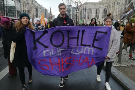 Demozug, im Vordergrund drei Menschen mit Transparent "Kohle nur zum Shishan"