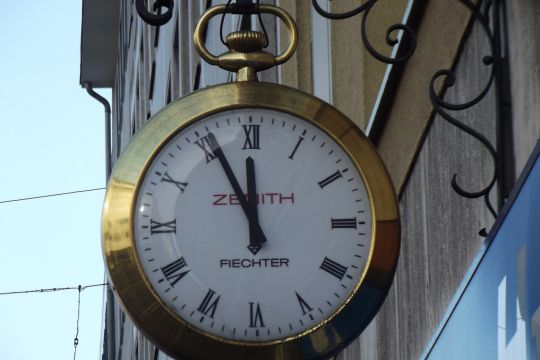 Eine Uhr an einem Laden zeigt fünf vor zwölf. 