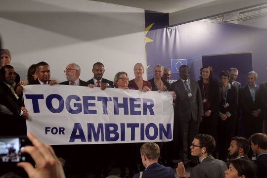 Minister stehen in einer Reihe und halten ein Transparent, auf dem "Together for Ambition" steht.